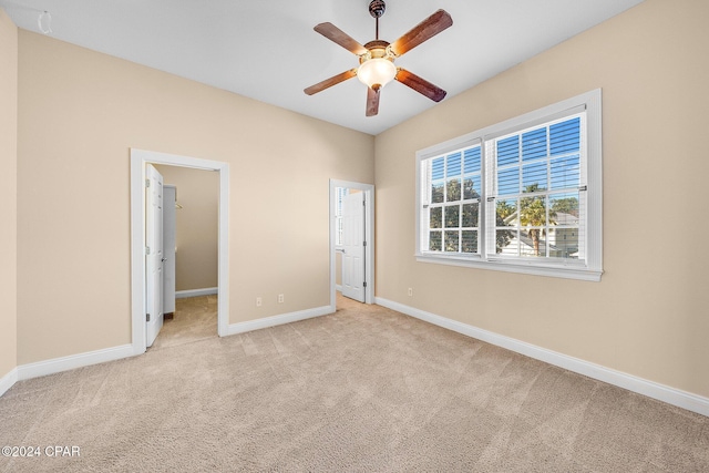 unfurnished bedroom with ceiling fan, a walk in closet, and light carpet