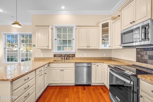 kitchen with appliances with stainless steel finishes, pendant lighting, sink, crown molding, and light hardwood / wood-style flooring