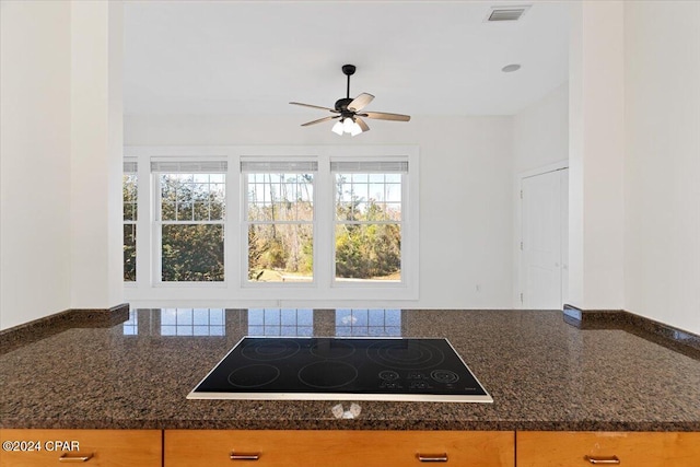 kitchen featuring black electric cooktop, ceiling fan, and dark stone countertops