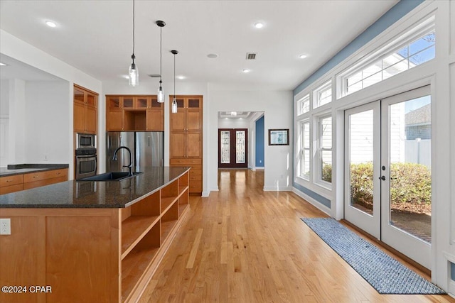 kitchen with french doors, appliances with stainless steel finishes, a kitchen island with sink, sink, and decorative light fixtures