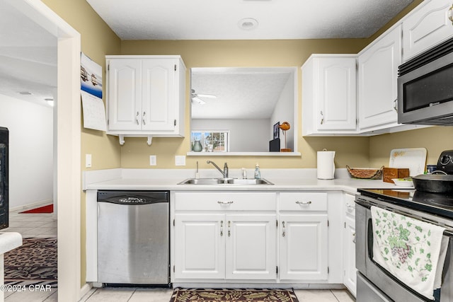 kitchen with a textured ceiling, white cabinets, stainless steel appliances, sink, and light tile patterned floors