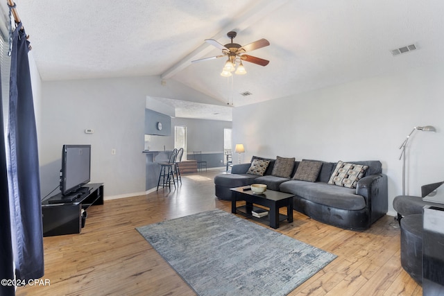 living room featuring ceiling fan, lofted ceiling with beams, a textured ceiling, and light wood-type flooring