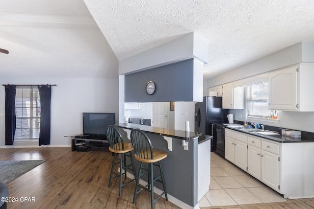 kitchen featuring kitchen peninsula, a breakfast bar, dishwasher, white cabinetry, and lofted ceiling