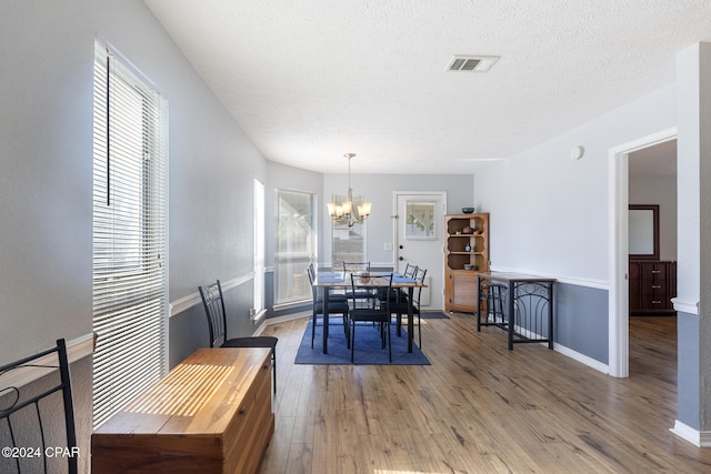 dining room featuring hardwood / wood-style flooring, a healthy amount of sunlight, a textured ceiling, and a chandelier