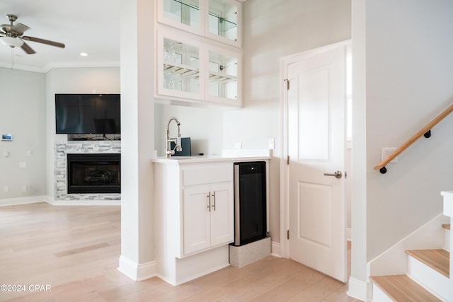 bar featuring white cabinets, a fireplace, wine cooler, ceiling fan, and light hardwood / wood-style flooring