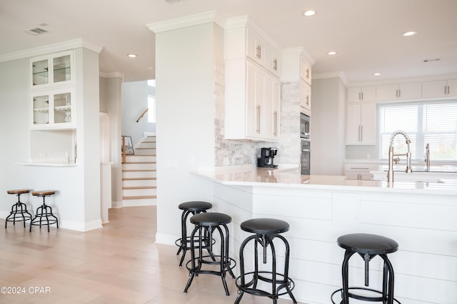 kitchen with tasteful backsplash, oven, white cabinetry, built in microwave, and a kitchen breakfast bar