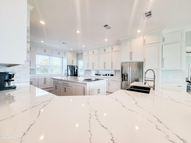 kitchen with light stone countertops, stainless steel fridge, white cabinets, and sink