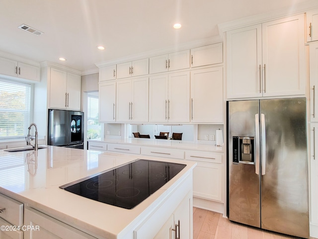 kitchen featuring black electric stovetop, white cabinetry, stainless steel fridge, and sink