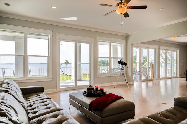 living room with ceiling fan, plenty of natural light, ornamental molding, and a water view