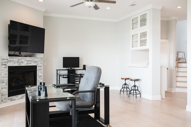 office area with ceiling fan, light wood-type flooring, crown molding, and a stone fireplace