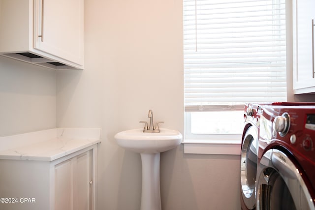 clothes washing area with plenty of natural light, sink, separate washer and dryer, and cabinets