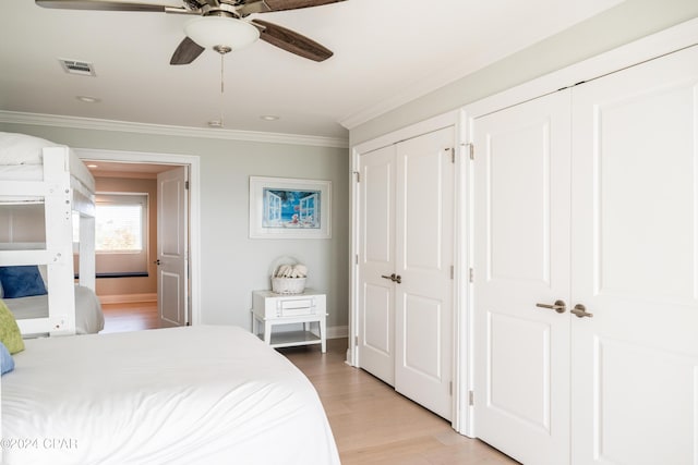 bedroom featuring ceiling fan, multiple closets, ornamental molding, and light hardwood / wood-style floors