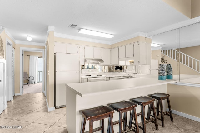 kitchen with white appliances, under cabinet range hood, a peninsula, light countertops, and a sink