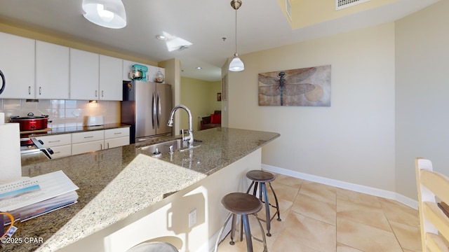 kitchen featuring sink, dark stone countertops, stainless steel fridge, pendant lighting, and a breakfast bar