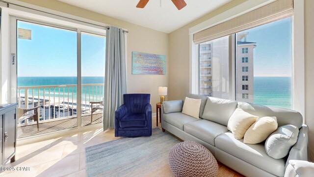 living room with a view of the beach, light tile patterned floors, a water view, and ceiling fan