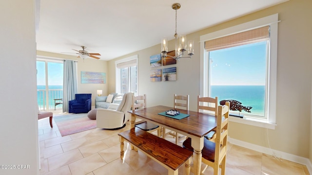 dining room featuring ceiling fan with notable chandelier, a water view, and light tile patterned floors