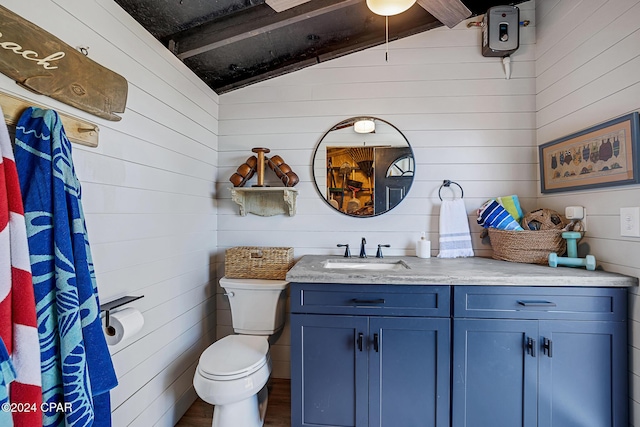 bathroom featuring vanity, toilet, lofted ceiling, and wooden walls