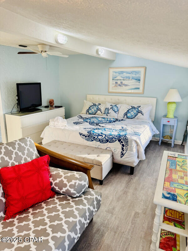 bedroom with a textured ceiling, ceiling fan, wood-type flooring, and vaulted ceiling