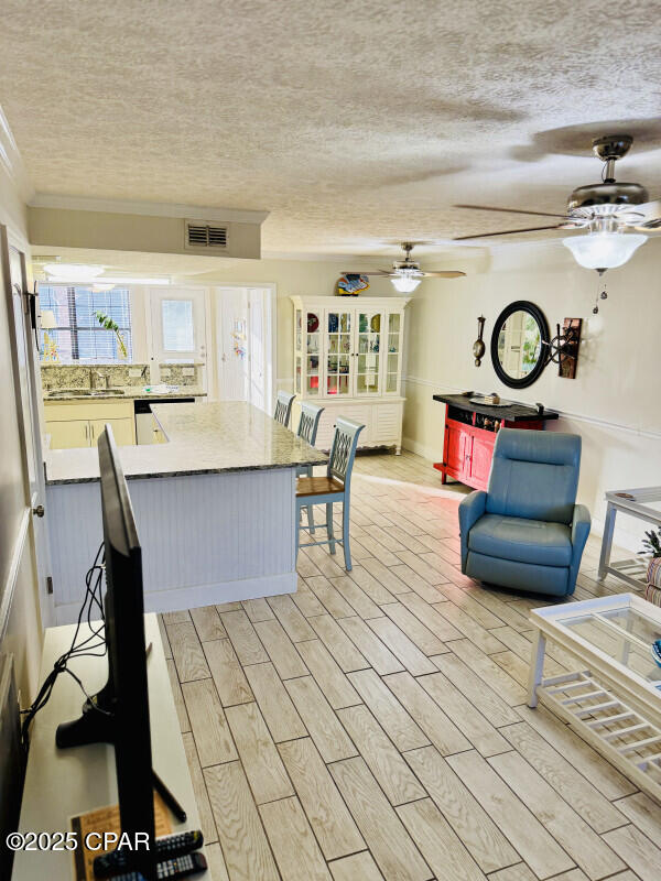 kitchen with crown molding, sink, a textured ceiling, and light wood-type flooring