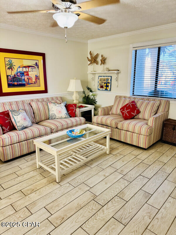 living room with crown molding, light hardwood / wood-style flooring, ceiling fan, and a textured ceiling