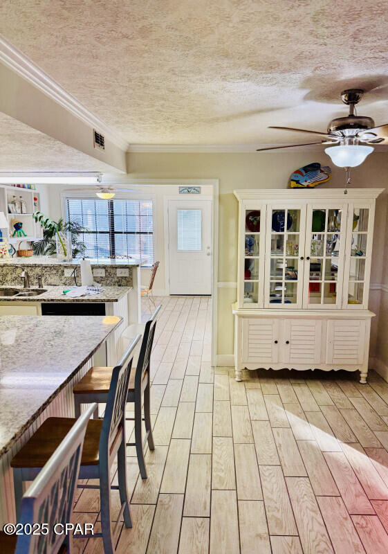 unfurnished dining area with sink, ceiling fan, ornamental molding, a textured ceiling, and light wood-type flooring