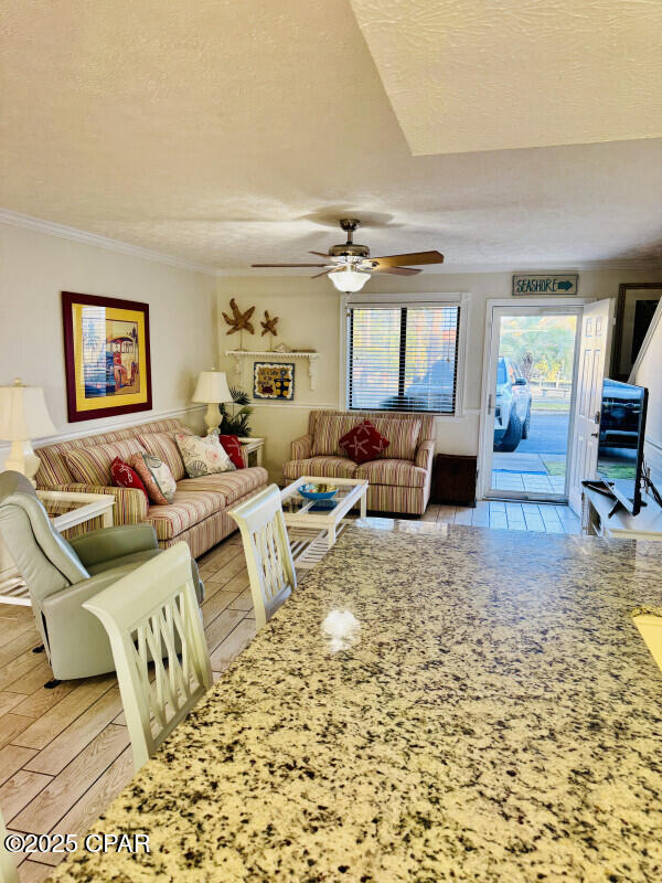 living room with ceiling fan, crown molding, a textured ceiling, and light wood-type flooring