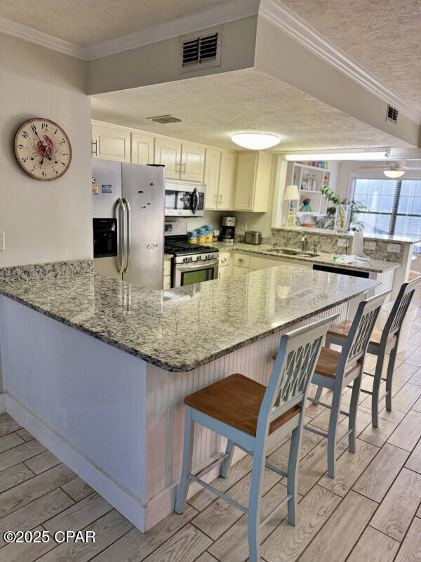 kitchen featuring kitchen peninsula, appliances with stainless steel finishes, light stone counters, a breakfast bar, and white cabinets