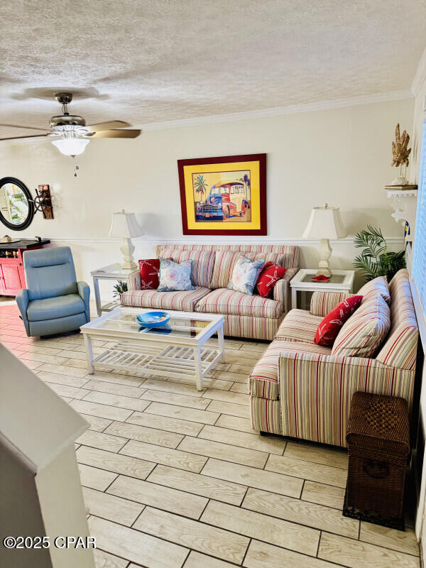 living room with crown molding, ceiling fan, and a textured ceiling