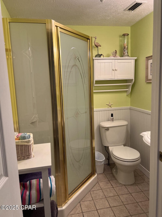 bathroom featuring tile patterned floors, a textured ceiling, toilet, a shower with shower door, and wood walls