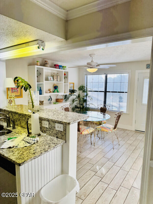 kitchen with light stone countertops, kitchen peninsula, ornamental molding, ceiling fan, and sink