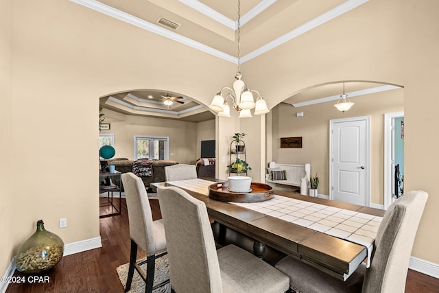 dining area with dark wood-type flooring, ceiling fan with notable chandelier, a tray ceiling, and ornamental molding