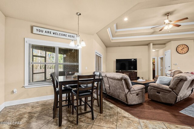 tiled dining room featuring ceiling fan with notable chandelier and a raised ceiling