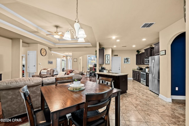 tiled dining room featuring ceiling fan with notable chandelier, a raised ceiling, and sink