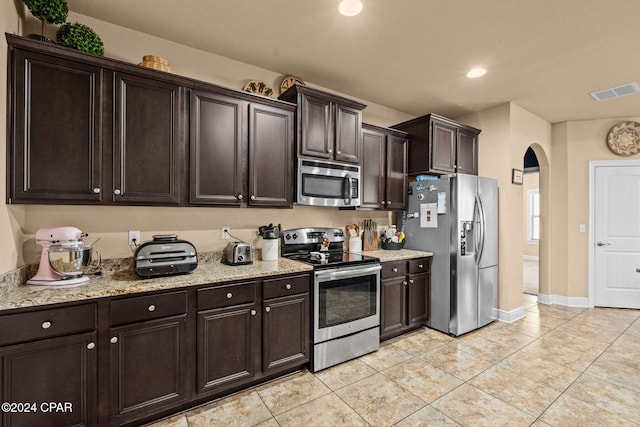 kitchen featuring light stone counters, dark brown cabinets, light tile patterned flooring, and appliances with stainless steel finishes