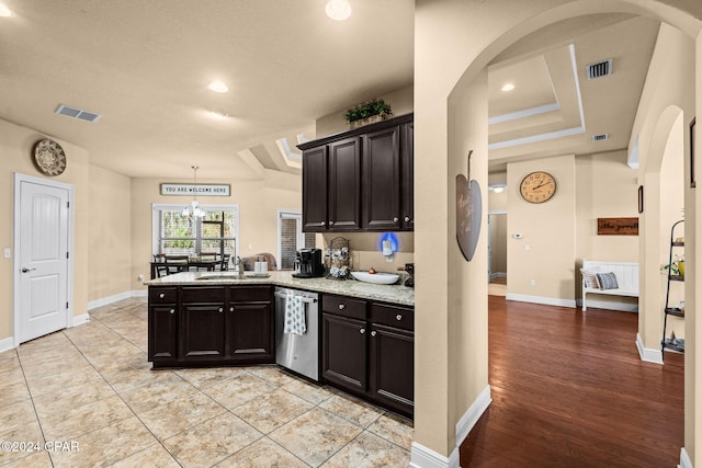 kitchen with a chandelier, a raised ceiling, stainless steel dishwasher, and sink