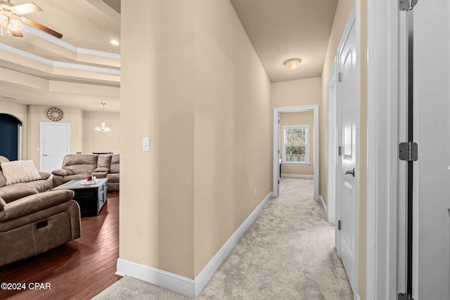 hall with carpet, a raised ceiling, an inviting chandelier, and ornamental molding