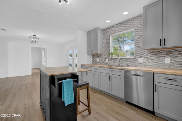 kitchen with butcher block counters, gray cabinetry, dishwasher, sink, and a breakfast bar