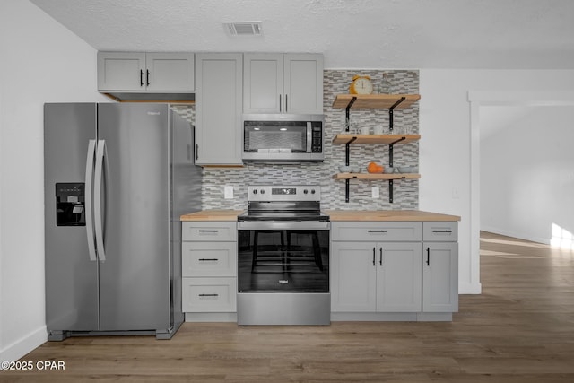 kitchen with decorative backsplash, appliances with stainless steel finishes, butcher block countertops, and light hardwood / wood-style floors