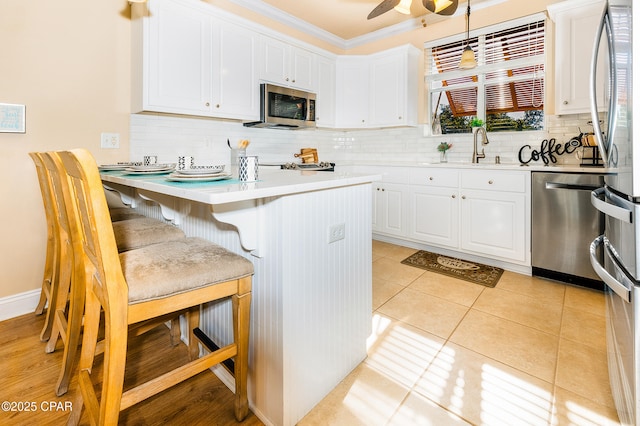 kitchen with a kitchen breakfast bar, stainless steel appliances, sink, light tile patterned floors, and white cabinetry