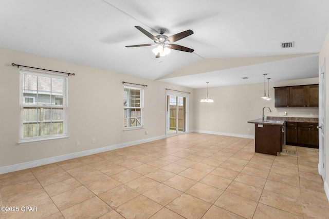 unfurnished living room featuring ceiling fan with notable chandelier, light tile patterned floors, sink, and vaulted ceiling