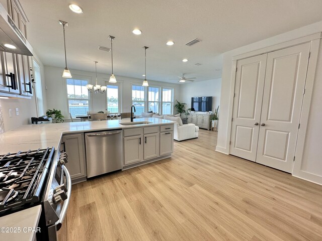 kitchen with decorative light fixtures, kitchen peninsula, sink, light hardwood / wood-style flooring, and stainless steel appliances