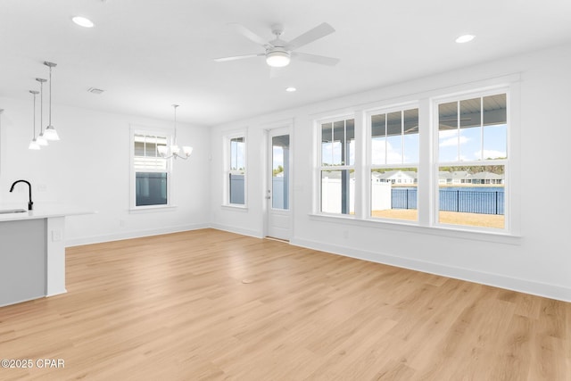 unfurnished living room with ceiling fan with notable chandelier, sink, and light hardwood / wood-style flooring