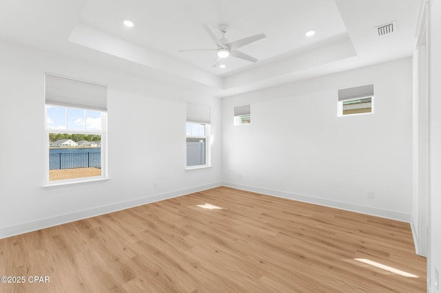 spare room featuring a raised ceiling, light wood-type flooring, and ceiling fan