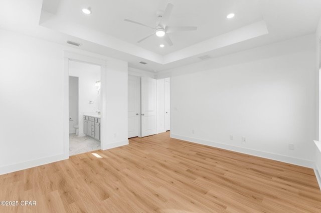 unfurnished bedroom with light hardwood / wood-style floors, ensuite bath, a raised ceiling, and ceiling fan