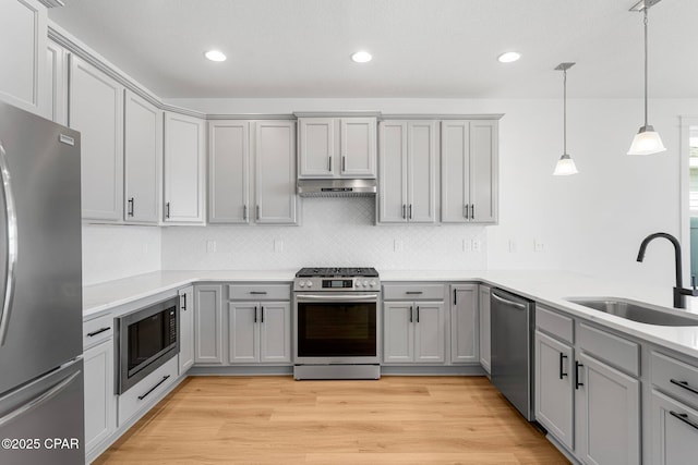 kitchen with decorative light fixtures, gray cabinets, sink, light hardwood / wood-style flooring, and appliances with stainless steel finishes