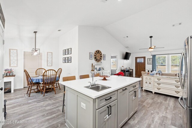 kitchen featuring a kitchen island with sink, sink, hanging light fixtures, ceiling fan, and stainless steel fridge