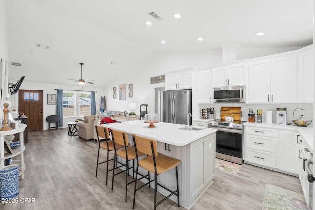 kitchen featuring a breakfast bar, a kitchen island with sink, white cabinets, ceiling fan, and stainless steel appliances