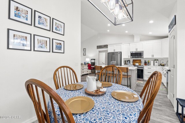 dining area with a notable chandelier, light hardwood / wood-style floors, and lofted ceiling