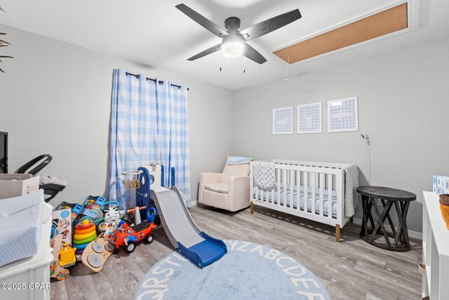 bedroom with ceiling fan, a crib, and light wood-type flooring