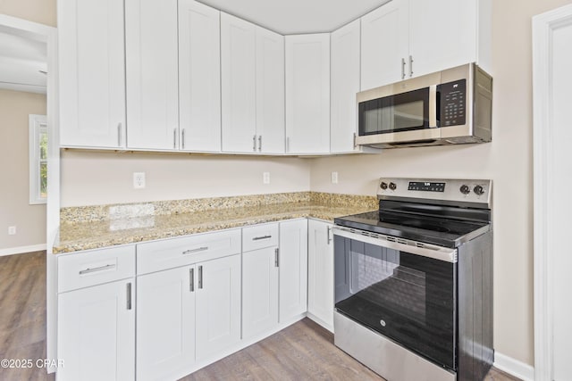 kitchen featuring white cabinetry, stainless steel appliances, light stone counters, and hardwood / wood-style flooring